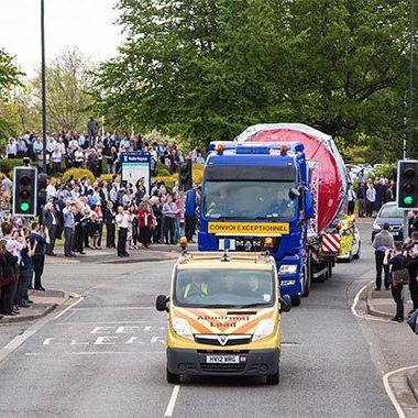 Large truck transporting a Rolls Royce Aero Engine, with a crowd watching from the roadside. Convoi Exceptionnel Escort vehicle. Large truck transporting a Rolls Royce Aero Engine, with a crowd watching from the roadside. Convoi Exceptionnel Escort vehicle.